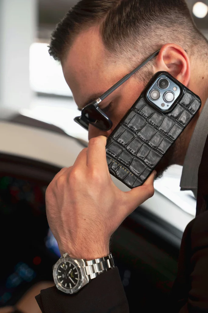 Ein stilvoller Mann mit einer eleganten Luxus-Armbanduhr, der ein Smartphone hält, symbolisiert Kommunikation und Exklusivität.