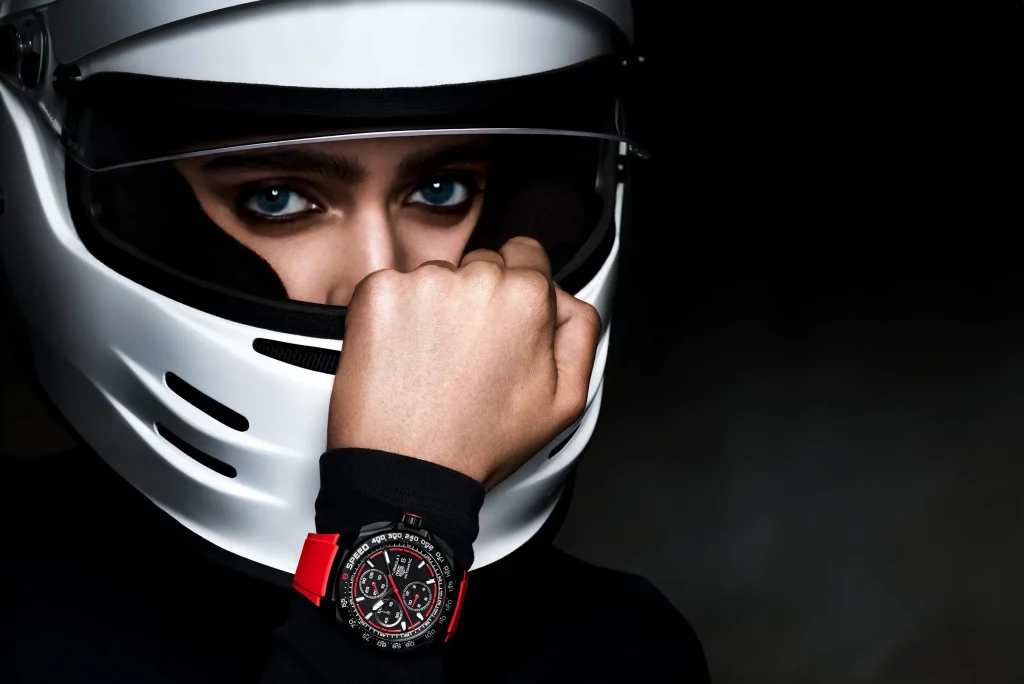 Rennfahrerin trägt den TAG Heuer Formula 1 Chronograph mit schwarzem Gehäuse und rotem Rand, während sie einen Helm trägt, im Motorsport-Stil.