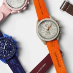 Mehrere MoonSwatch-Uhren mit verschiedenen bi-color Kautschukarmbändern, die in einer Auswahl von Farben wie Navyblau/Blau, Rot/Weiß, Orange/Sand und anderen präsentiert werden. Perfekte Kombination aus Stil und Funktionalität.