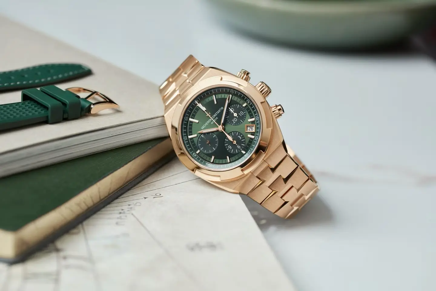 Goldene Vacheron Constantin Overseas mit grünem Zifferblatt, stilvoll auf einem Tisch arrangiert.